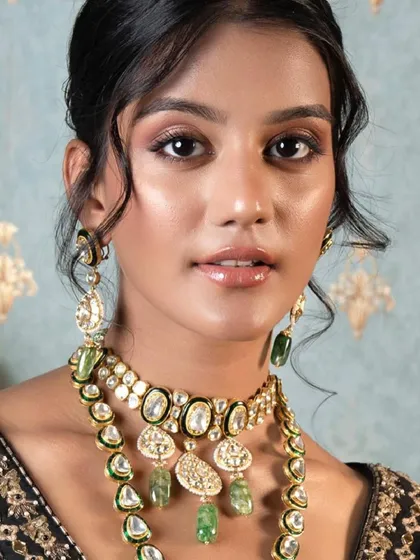 A beauty shot highlighting a gorgeous polki and emerald jewellery set. The soft makeup and elegant updo ensure the focus remains on the intricate details of the necklace and earrings, perfect for a bride's reception look.
