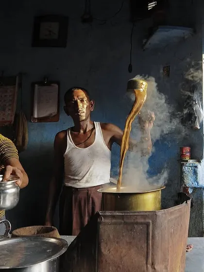 In a small tea stall, a chaiwala expertly pulls tea, a daily ritual that fuels the community. This candid shot captures a slice of everyday life and commerce within the bustling lanes.