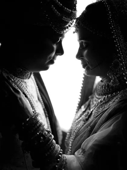 An intimate, high-contrast silhouette of the bride and groom. This artistic shot focuses on their connection, using light and shadow to create a classic wedding portrait.