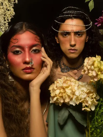 Another look from the floral-themed editorial, featuring a bold red facial makeup concept. The hair is styled with soft, wet-look waves to frame the face and the intricate jewelry.