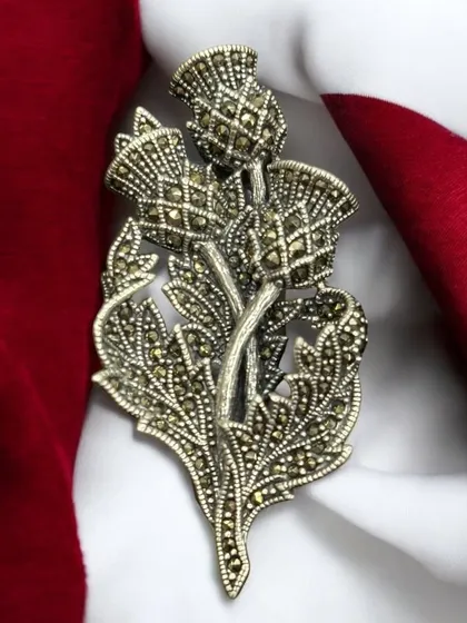 An exclusively unique silver brooch designed in the shape of a thistle flower. This piece is detailed with marcasite stones, giving it a vintage, sparkling appearance perfect for coats and sarees.