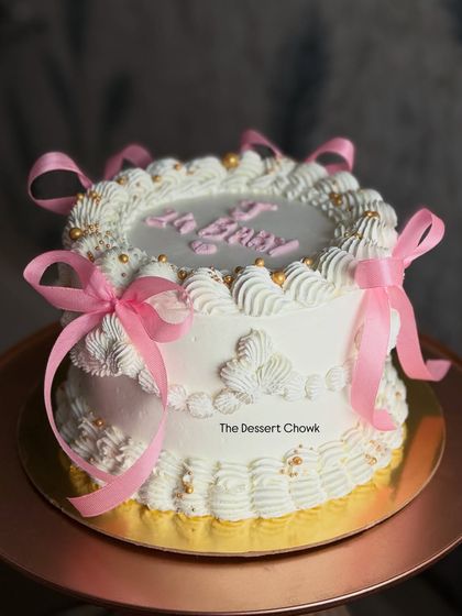 A beautiful vintage-style cake with pink ribbons, perfect for a baby shower. This was a Crunchy Vanilla flavor, a classic choice for a sweet celebration.