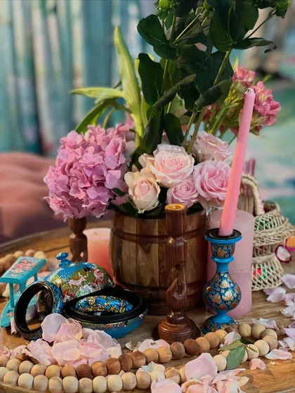 A tablescape reflecting the essence of Kashmir. The decor includes pink hydrangeas and roses, wooden beads, and hand-painted boxes, creating a rich and culturally inspired setting.