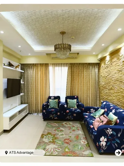 This living room combines floral sofas with a textured stone accent wall for a unique fusion of styles. The coffered ceiling with a chandelier adds a touch of classic elegance.