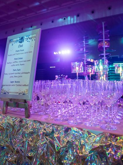 The bar area, where the iridescent theme continued. The bar front was wrapped in shimmering material, complemented by a custom menu and an elegant display of glassware, all under a soft purple glow.