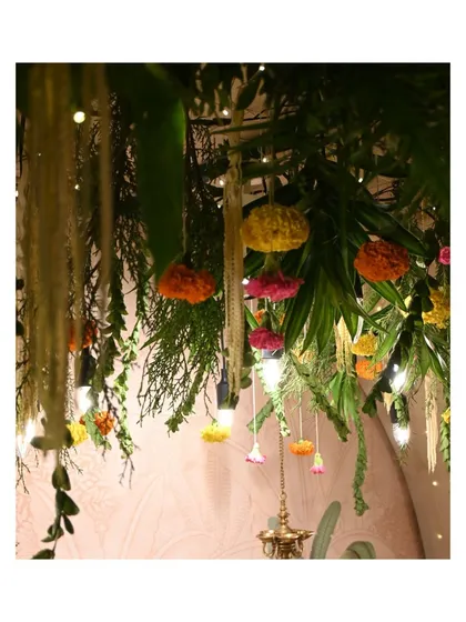 A detail shot of the overhead floral canopy we created for a Ganpati celebration. We combined fresh palm fronds, hanging marigolds, and delicate white flower strings with warm Edison bulbs to craft a rich, multi-layered, and festive ceiling treatment.