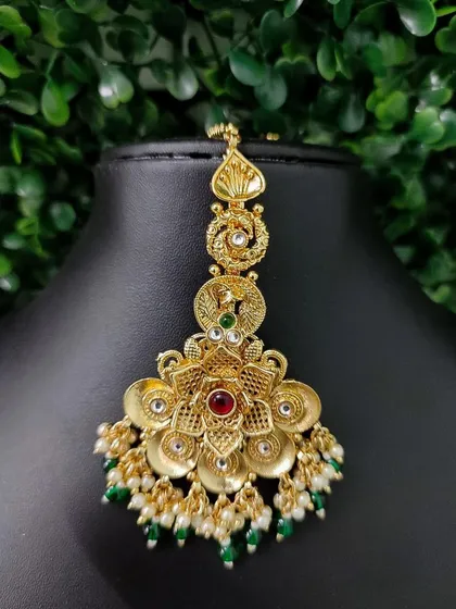 The right maang tikka is a game changer. This piece showcases intricate gold-tone floral metalwork, studded with kundan and finished with delicate pearl and green beads.