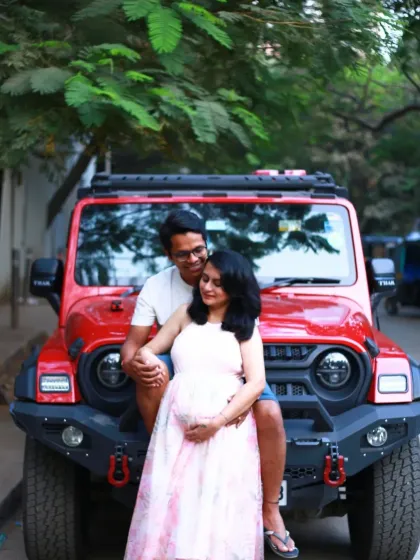 A cool, modern maternity shot with the couple posing on the front of a red jeep, blending urban style with the joy of expectancy.