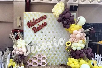 This "Welcome Babee" backdrop features a honeycomb pattern and is framed by a unique balloon garland. The use of pampas grass and sunflowers adds a rustic, boho touch to the bee-themed baby shower.