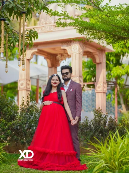 A sophisticated couple's portrait in a lush garden. The vibrant red gown stands out beautifully against the green foliage and elegant gazebo.