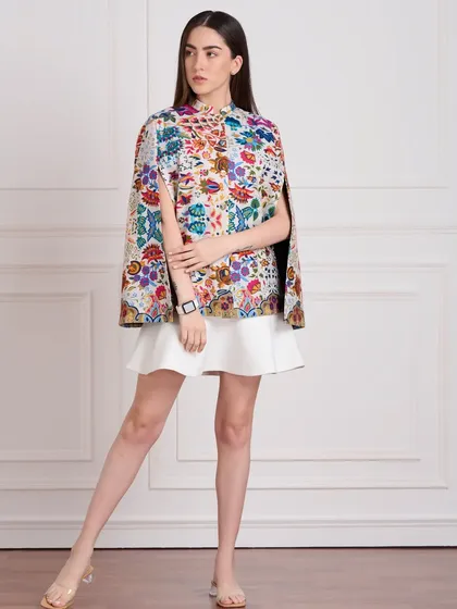 A full-length e-commerce shot of a model wearing a colorful printed cape. The simple pose and neutral background ensure that the focus is entirely on the product's design and fit.