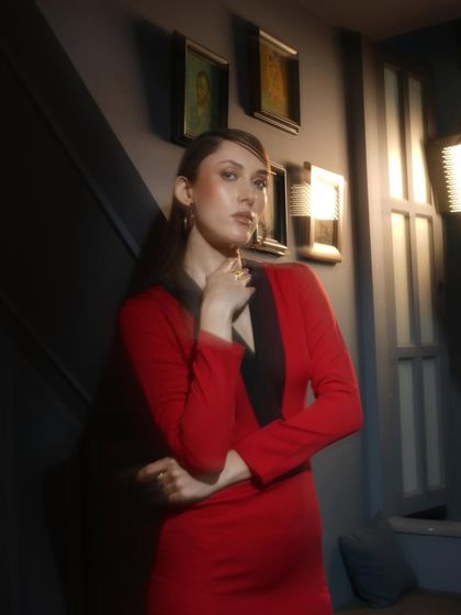A moody shot of a model in a bold red dress with black lapels. The lighting is dramatic, creating deep shadows that add to the mysterious and sophisticated vibe.