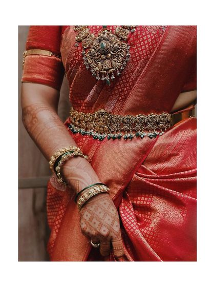 A detailed shot of the bride's waist, showcasing her intricate gold belt (oddiyanam) and the rich texture of her red silk saree.