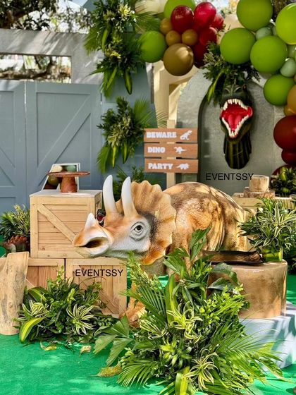 A life-sized triceratops prop creates a huge 'wow' moment, complemented by wooden crates and a 'Beware Dino Party' sign.