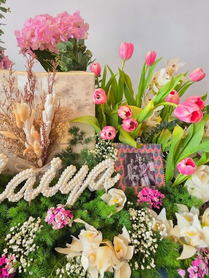 A close-up of the 'Maiya' hamper, showing the intricate pearl lettering and a framed family photo nestled among the fresh flowers.