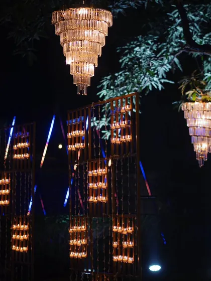 An artful installation of candle walls and hanging crystal chandeliers amidst the trees, blending structured light with nature.