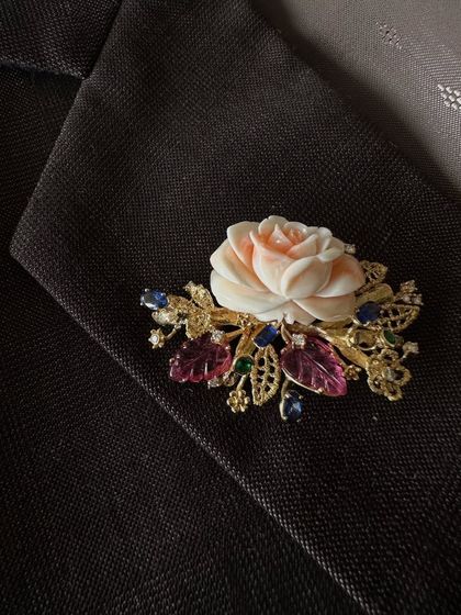 This unique brooch features a hand carved coral rose, set amongst leaves made of carved tourmalines and sapphires. It is a celebration of different materials and craftsmanship, a true piece of art.