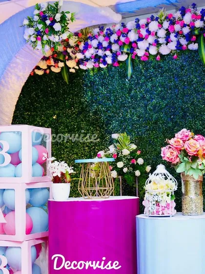 A closer look at the modern baby shower setup, highlighting the floral arrangements and decorative props. The combination of a green wall, pastel arch, and balloon boxes creates a fresh and stylish look.