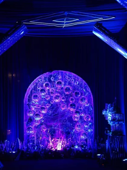 A dramatic entrance featuring a peacock-inspired, back-lit structure, framed by geometric illuminated arches in electric blue and violet.