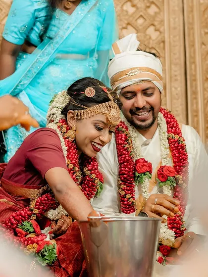 A fun and candid moment from a South Indian wedding, where the couple playfully searches for a ring in a pot of water.