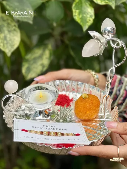 A complete Raksha Bandhan set, this leaf-shaped silver-plated thali is adorned with a crystal floral accent. It comes ready with a diya, a rakhi, and space for sweets, making the celebration effortless and beautiful.
