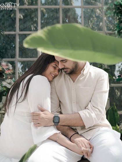 A tender moment captured in a sun-drenched greenhouse. The soft light and abundance of plants create a serene and intimate setting, with the large leaf providing beautiful natural framing.