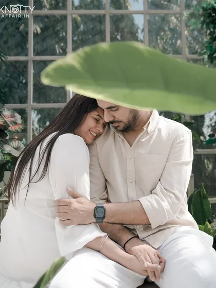 A tender moment captured in a sun-drenched greenhouse. The soft light and abundance of plants create a serene and intimate setting, with the large leaf providing beautiful natural framing.