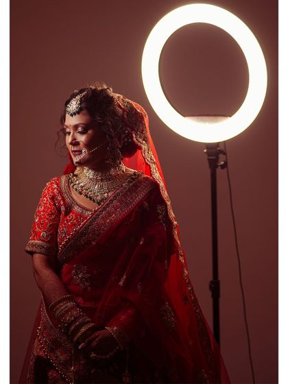 A modern take on a bridal portrait, using a ring light to create a unique halo effect. This image highlights the bride's stunning red lehenga and her calm, collected presence before the ceremony.