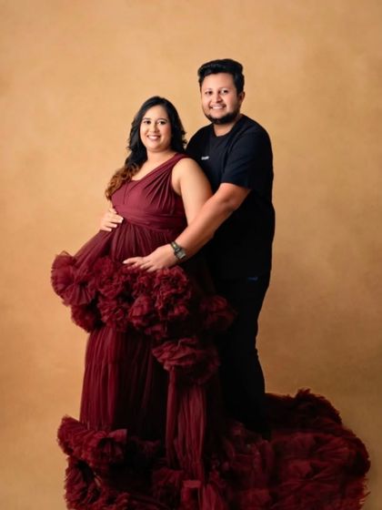 A happy and smiling couple's portrait, with the mom-to-be in our rich burgundy ruffled gown.