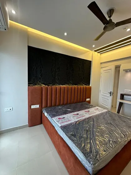 A newly installed bedroom featuring a striking black textured panel behind a rust-colored, channel-tufted headboard. The cove lighting in the false ceiling adds warmth and highlights the different textures.
