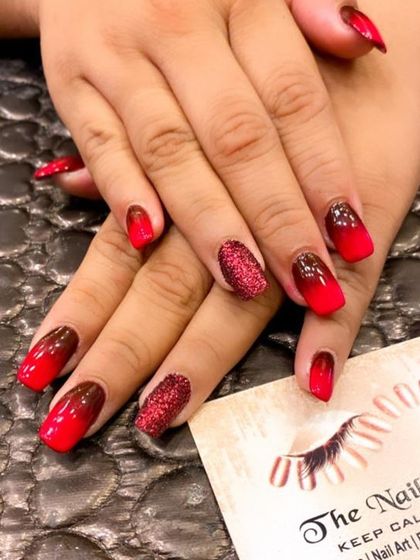 A fiery and dramatic ombre on square-shaped nails. The design fades from a deep maroon to a bright red, with accent nails covered in sparkling red glitter.