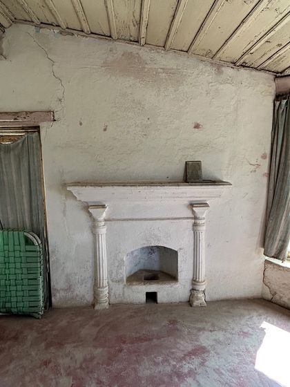 The interior of Verdun House before restoration, with a crumbling fireplace, stained floors, and makeshift curtains, showing the extent of the decay.