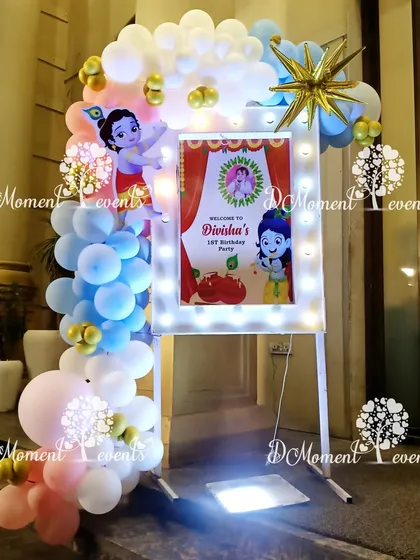 A lighted welcome sign for Divisha's first birthday party. The sign is framed with pastel balloons and features cute illustrations of Little Krishna.