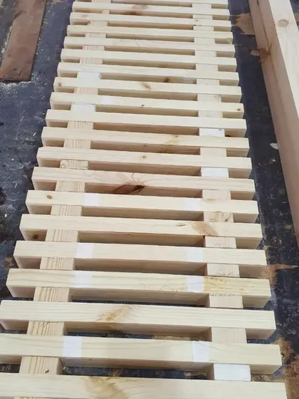 The assembly process begins. The slatted top of the bench is being glued and clamped, using spacers to ensure uniform gaps between each piece of wood.