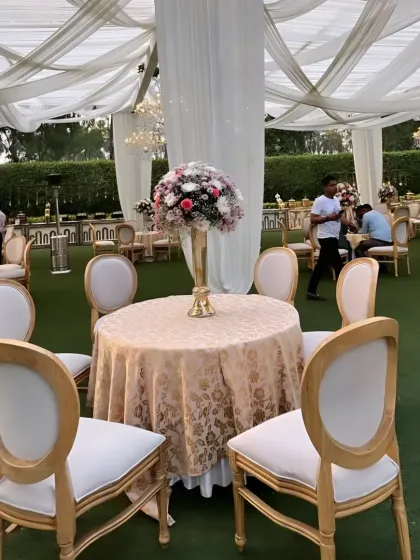 Classic and elegant seating for an outdoor luncheon. The gold and white chairs paired with a patterned tablecloth and a tall floral centerpiece create a timeless and sophisticated look.