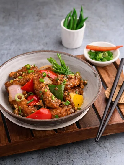 A classic Chicken Chilli from Bombay Diner, styled with fresh peppers and spring onions. The composition is clean and focuses on the vibrant colors of the dish.