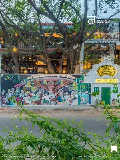 The exterior of Adda 1522 at night, showcasing a large, vibrant mural that captures the spirit of Bangalore. The design respects the existing trees on the property, integrating the building with its natural surroundings.