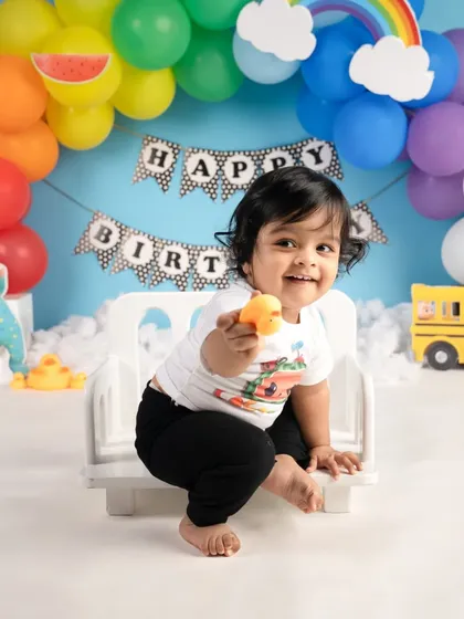 A big, happy smile from the birthday boy during his Cocomelon-themed shoot. The colorful balloons and props make the scene so vibrant.
