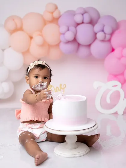 This one-year-old is enjoying her pastel-themed cake smash. The soft colors of the balloons and her outfit create a sweet and gentle look.