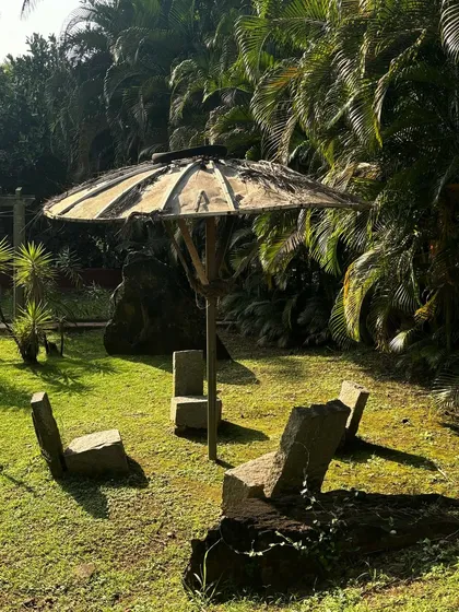 A serene garden scene with stone chairs and a unique umbrella-like structure, surrounded by dense greenery. This image captures the harmony of life and the peace found in a well-designed natural landscape.