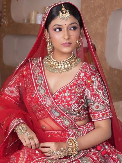 A classic red bridal look featuring a Kundan choker with light green bead drops, a matching maang tikka, and a traditional nath. This set is perfect for the quintessential Indian bride.