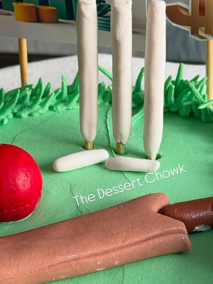 A close-up of the fondant cricket pitch, complete with a leather ball, bat, and wickets.