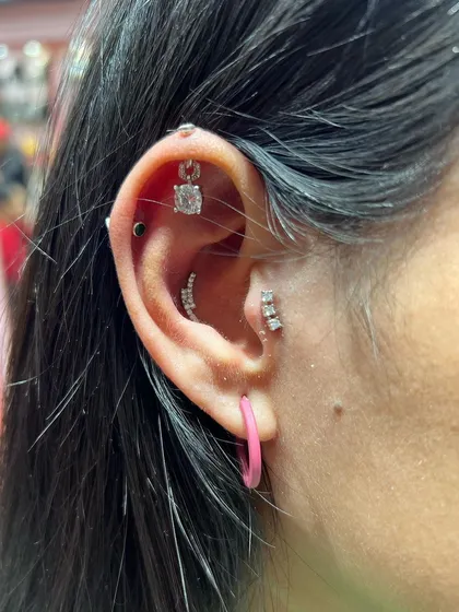 A modern and edgy ear stack with a square solitaire hanging, multiple bar studs, and a pop of color from a pink hoop.