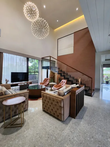 We designed this double-height living room to feel like a private resort, using expansive windows and grand chandeliers to create a sense of scale and tranquility. The space is anchored by a terracotta-colored feature wall and a modern staircase, blending warmth with contemporary design.