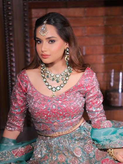 A regal pose in a stunning pink and teal lehenga. The makeup is kept soft and elegant to balance the vibrant colours and heavy embroidery of the outfit.