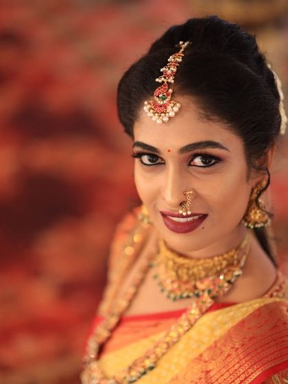 A close-up of Sahana's beautiful smile and her traditional maang tikka. The details of her temple choker are also visible, completing the look.