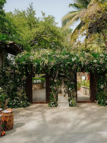 The main gates are completely covered in lush greenery and white flowers, creating a magical, overgrown garden entrance for guests.