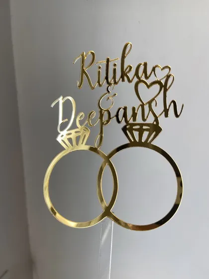 Celebrate your engagement with a design that says it all. This "Ritika & Deepansh" topper features interlocking rings and elegant script, making it a popular choice for couples starting their new journey.