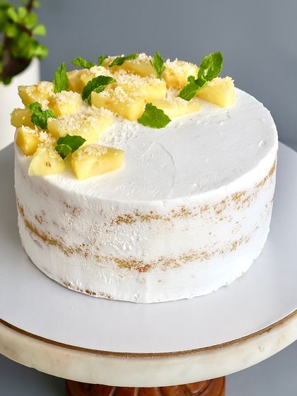A tropical escape in every slice. This Coconut Pineapple Naked Cake combines a soft coconut vanilla sponge with a tangy pineapple compote and fresh pineapple chunks. It's light, refreshing, and made with the finest ingredients.