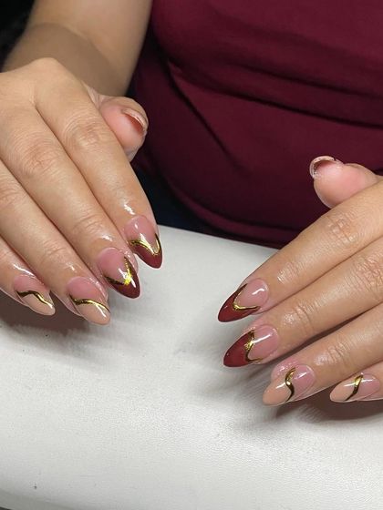 A beautiful design with a deep red French tip and a delicate gold swirl on a nude base.